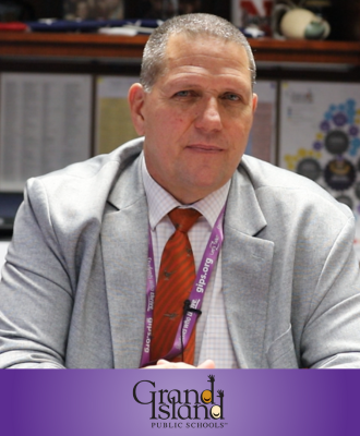  Mr. Fisher in a suit and tie sitting at his desk with the GIPS logo over a purple footer. 