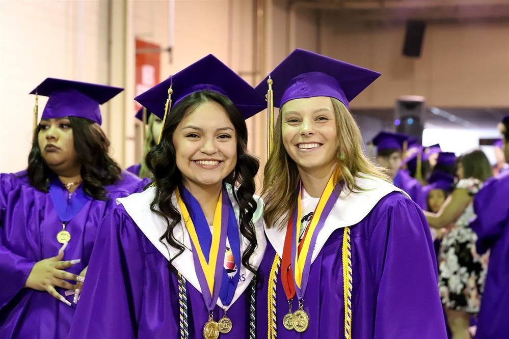Two GISH graduates smiling in their graduation regalia. 
