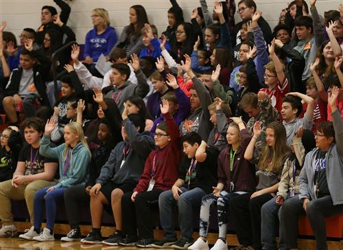 Barr Middle School students raising their hands while sitting on benches in the gym