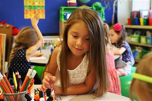 Smiling Kindergarten student leaning on a desk with colors and pencils