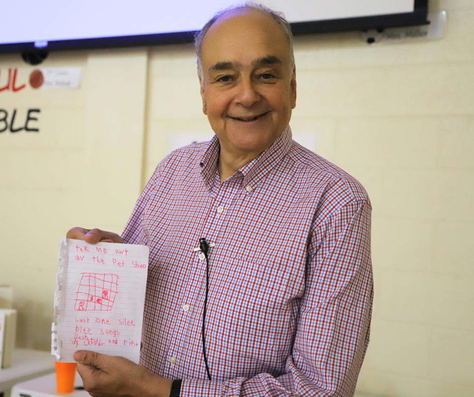 Alan Katz smiling with a copy of an original song written to him by an Engleman 1st Grader.