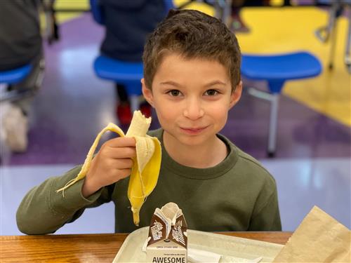 Image of smiling student eating a banana in a GIPS lunch room