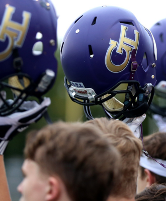  GISH football players holding up their purple and gold helmets at a game.