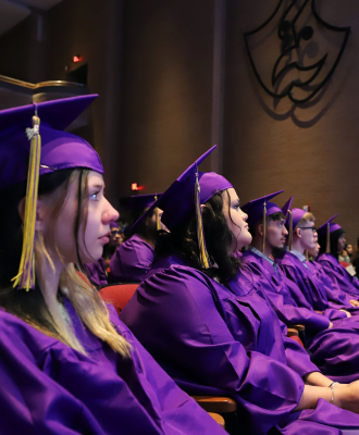  Row of GISH Graduates in purple regalia listening to the midterm graduation ceremony program