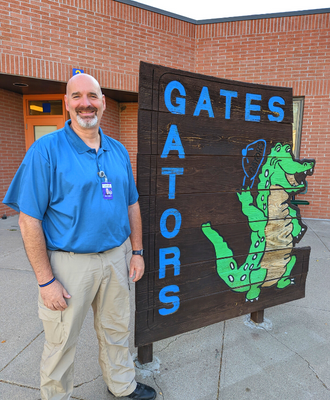  Mr. Wes Tjaden standing and smiling outside Gates Elementary next to the school sign.